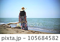 Romantic woman sitting alone is watching the sea view on overturned dry tree trunk on beach. Then she gets up and walks on the seashore. 105684582