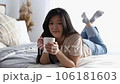 Happy asian woman in casual clothes holding mug lying on the bed at home 106181603