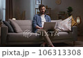 Man looking at screen and talking. Male wearing headphones. Man conducting video conference. Man using laptop and headset. Male sitting at couch at living room. Male joining online meeting. 106313308