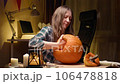 Preparing pumpkin for Halloween. Woman sitting and pulling out face details of carved halloween Jack O Lantern pumpkin at home for her family. 106478818