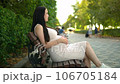 A pregnant woman sitting on a crowded bench, tenderly caressing her belly amid the hustle and bustle of a public place. 106705184