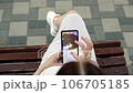 In a bustling public place, a pregnant young woman sits on a bench, deeply engrossed in examining an ultrasound photo of her baby on her smartphone. 106705185