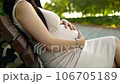 A pregnant woman sitting on a crowded bench, tenderly caressing her belly amid the hustle and bustle of a public place. 106705189