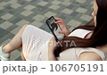 In a bustling public place, a pregnant young woman sits on a bench, deeply engrossed in examining an ultrasound photo of her baby on her smartphone. 106705191