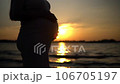A poignant moment unfolds the silhouette of a pregnant woman cherishes her belly amidst the backdrop of a serene waterscape and the descending sun 106705197