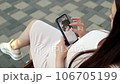 In a bustling public place, a pregnant young woman sits on a bench, deeply engrossed in examining an ultrasound photo of her baby on her smartphone. 106705199