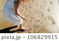 Girl child drawing with a stick on the sand on the beach and having fun 106829915