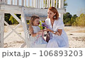 Mom and daughter in white dresses spend time together on the beach and have fun 106893203