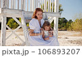 Mom and daughter in white dresses spend time together on the beach and have fun 106893207