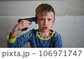 Boy playing with a toy gun. Child holds a toy gun to his temple. Entertainment for children 106971747