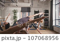 Group of people doing body stretching in fitness room. Standing on mats performing exercises of bending body to side. Rejuvenation of their body and improving of blood circulation. 107068956