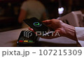An old woman pays for purchases, contactless with a smartphone, NFC technology. Senior female puts the phone to the pos terminal in a cafe 107215309