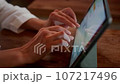 Close-up: female hands typing on a tablet screen in a cafe. The wrinkled fingers of the female touch the touchscreen in the coffee shop 107217496