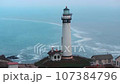 Lighthouse on the ocean shore in rainy coastal weather. 107384796