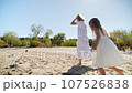 Mom and daughter in white dresses running on the beach and laughing 107526838