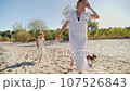 Mom and daughter in white dresses running on the beach and laughing 107526843