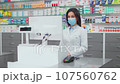 Female pharmacist looking at computer screen. Woman pharmacist working with cash register. Woman wearing robe and mask at background of showcase with medicine. Caucasian pharmacist in drugstore. 107560762