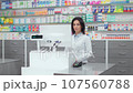 Female pharmacist looking at computer monitor. Woman pharmacist working with cash register. Woman in white robe standing at background of showcase with medicine. Caucasian pharmacist in drugstore. 107560788