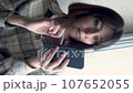 vertical video a young brunette near the window writes a message on a smartphone searches for information on the Internet. close-up 107652055