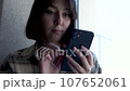a young brunette near the window writes a message on a smartphone. close-up 107652061