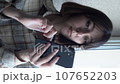 vertical video a young brunette near the window writes a message on a smartphone searches for information on the Internet. close-up 107652203