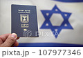 Hand holds an Israeli international passport against the Israeli flag waving in the wind 107977346