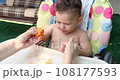 a small child sits on a baby feeding chair and eats a peach in the summer. Childhood concept. Close-up shot 108177593