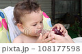 a small child sits on a baby feeding chair and eats a peach in the summer. Childhood concept. Close-up shot 108177598