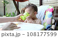 Portrait of a little boy who sits on a child's chair. Happy child drinks milk, kefir or dairy products from a cup. Correct and natural nutrition for children 108177599