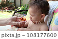 a small child sits on a baby feeding chair and eats a peach in the summer. Childhood concept. Close-up shot 108177600