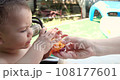 a small child sits on a baby feeding chair and eats a peach in the summer. Childhood concept. Close-up shot 108177601