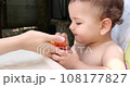 a small child sits on a baby feeding chair and eats a peach in the summer. Childhood concept. Close-up shot 108177827