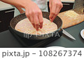 Spreading grated cheese into the pan on top of the sausage 108267374