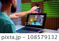 a young man takes pictures of himself on the phone and displays the video on the laptop screen 108579132