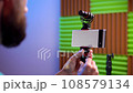 vlog setup with smarthone and microphone on tripod in vlogging studio. Led lights, softbox and phone on the table in living room. 108579134