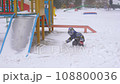 3 years old boy enjoying winter day on a fenced sports ground. He approaches the camera wrapped in a warm scarf. Fun winter holidays. Holiday outdoors in cold winter 108800036
