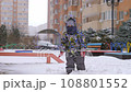 3 years old boy enjoying winter day on a fenced sports ground. He approaches the camera wrapped in a warm scarf. Fun winter holidays. Holiday outdoors in cold winter 108801552