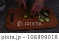 Close-up woman cuts cucumber on a wooden cutting board, 108899018
