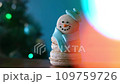 Snowman dessert macaron decorated with hat and scarf with colorful lights and flashing bokeh on foreground and Christmas tree on background. Merry Christmas and Happy New Year festive concept 109759726