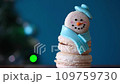 Snowman dessert macaron decorated with scarf and hat against Christmas tree with colorful lights and bokeh background. Camera moves away from object. Merry Christmas and Happy New Year festive concept 109759730