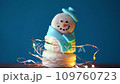 Snowman dessert macaron decorated with hat and scarf wrapped with colorful decorative flashing garland lights against blue background. Camera moves away from object. Merry Christmas and HNY concept 109760723