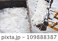 Close-up overhead above view of tractor loader machine snowplow shovel loading pile of snow and ice in dump truck for removal from city street at blizzard snowfall. Snow cleaning and removal 109888387