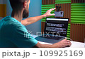 A young man shoots a video on a smartphone while reading text from a teleprompter on a laptop 109925169