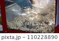 Classic popcorn machine with an unknown hand scooping fresh popcorn. Popcorn is poured into a bag for guests to enjoy. Manufacturer of popcorn and scoop 110228890
