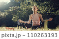 Front view of a young woman sitting on yoga mat in lotus position and deeply breathing. Beautiful girl practicing yoga at the morning sunlight outdoors at the city park Perfect footage for mindfulness 110263193