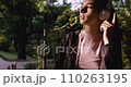 Woman in headphones walking nature at summer weekend close up. Attractive serene girl listening music in earphones strolling beautiful park. Relaxed carefree lady raising hands dancing along song. 110263195