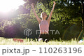 Woman doing hands and meditation pose for yoga practice surrounded by green park, forest, and big tree. Woman enjoy yoga at park. 110263196