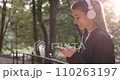Young cheerful active sporty girl walking with headphones mobile phone enjoying listening to music, jogging outdoors on urban city park or forest background. Woman makes fitness workout earphones 110263197