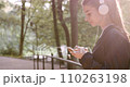 Calm woman in earphones walking green sunny forest looking smartphone screen close up. Beautiful girl listening music in headphones using cellphone application. Romantic lady enjoying summer weekend. 110263198