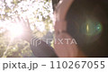 Sun shines through woman's hand while she holds it among green leaves in the forest 110267055